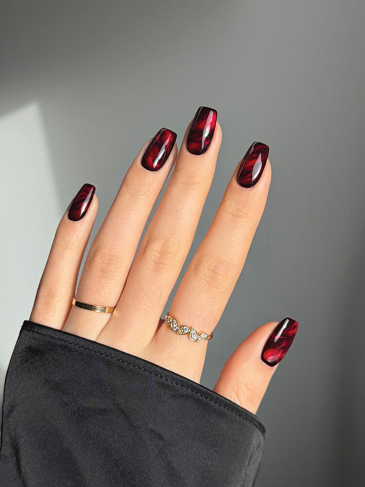 A hand peeks out from a black sleeve to reveal a red and black marbleized nail design by artist Sarah Haidar.
