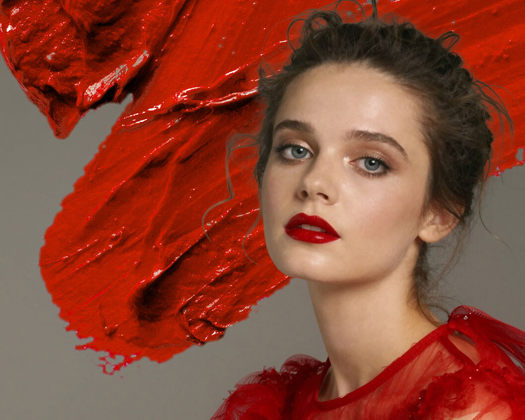 The model with the updo, red sequin party gown and a shiny red pout sits in front of a z-shaped smear of orangey red lipstick.