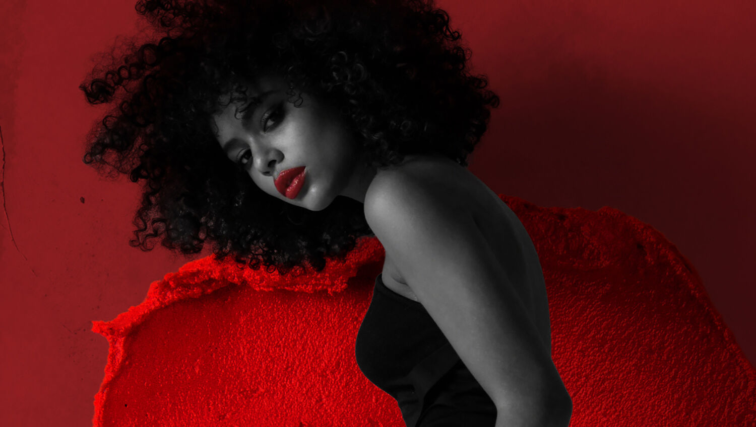 A model is pictured in black and white against a cherry background that includes a smudge of lipstick with only her mouth colored bright with red lipstick.