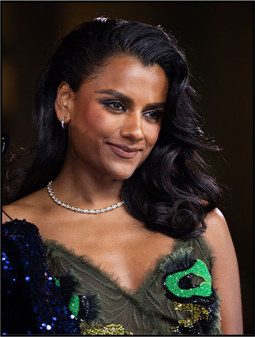 Close‑up of Simone Ashley with hair slicked back on one side and worn down on the other, showcasing diamond earrings and a matching necklace.
