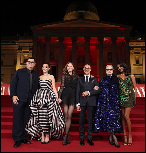 Caleb Hearon, Anne Hathaway, Emily Blunt, Stanley Tucci, Meryl Streep, and Simone Ashley stand together on the steps of Trafalgar Square with the National Gallery behind them.