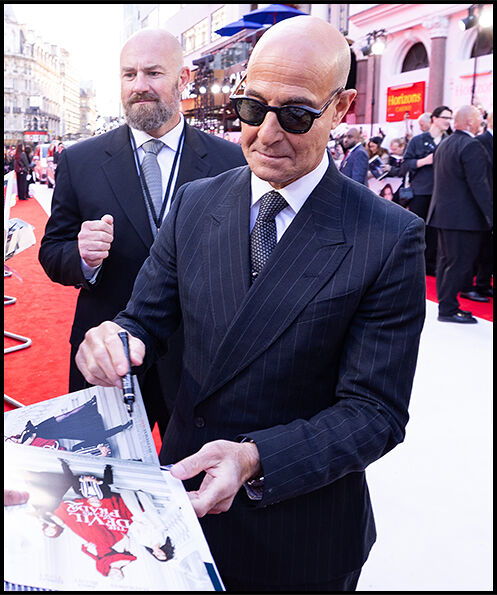 Stanley Tucci signs a The Devil Wears Prada 2 poster for a fan while walking the red carpet.