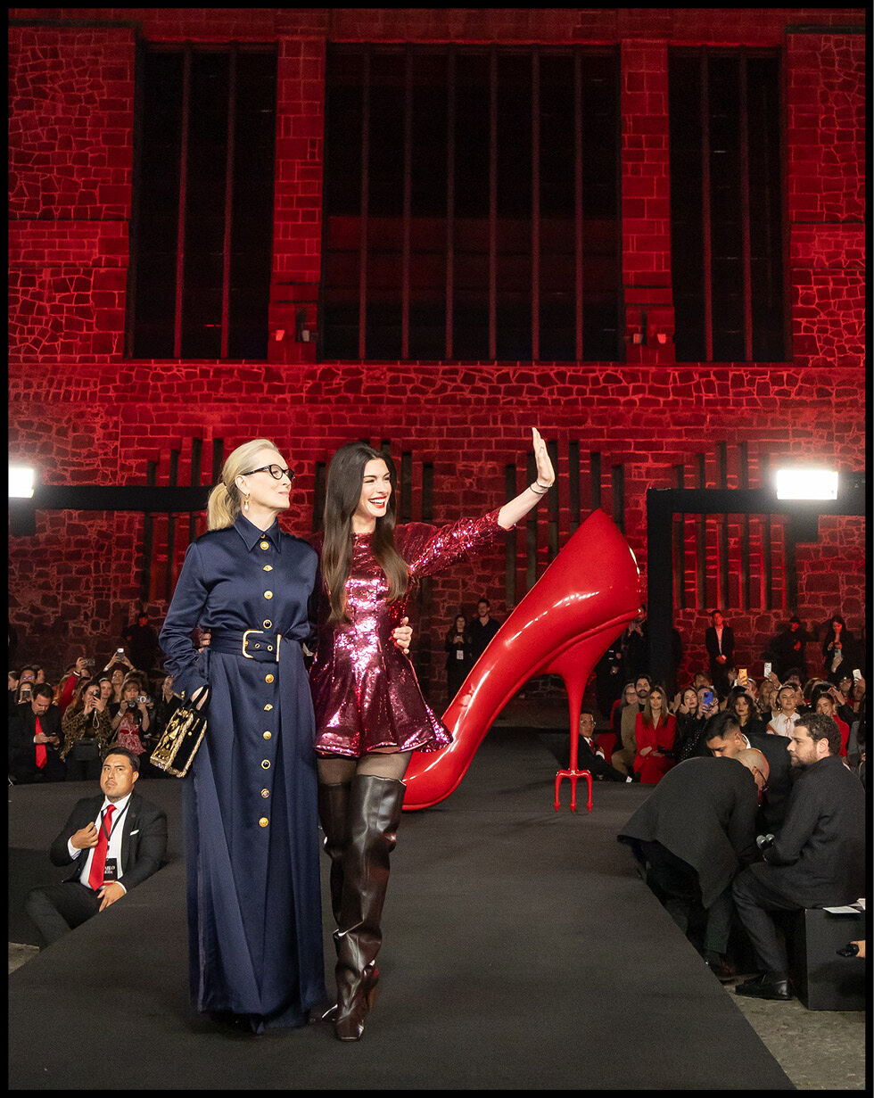 Anne Hathaway and Meryl Streep smile at a crowd in front of an oversized red heel. 