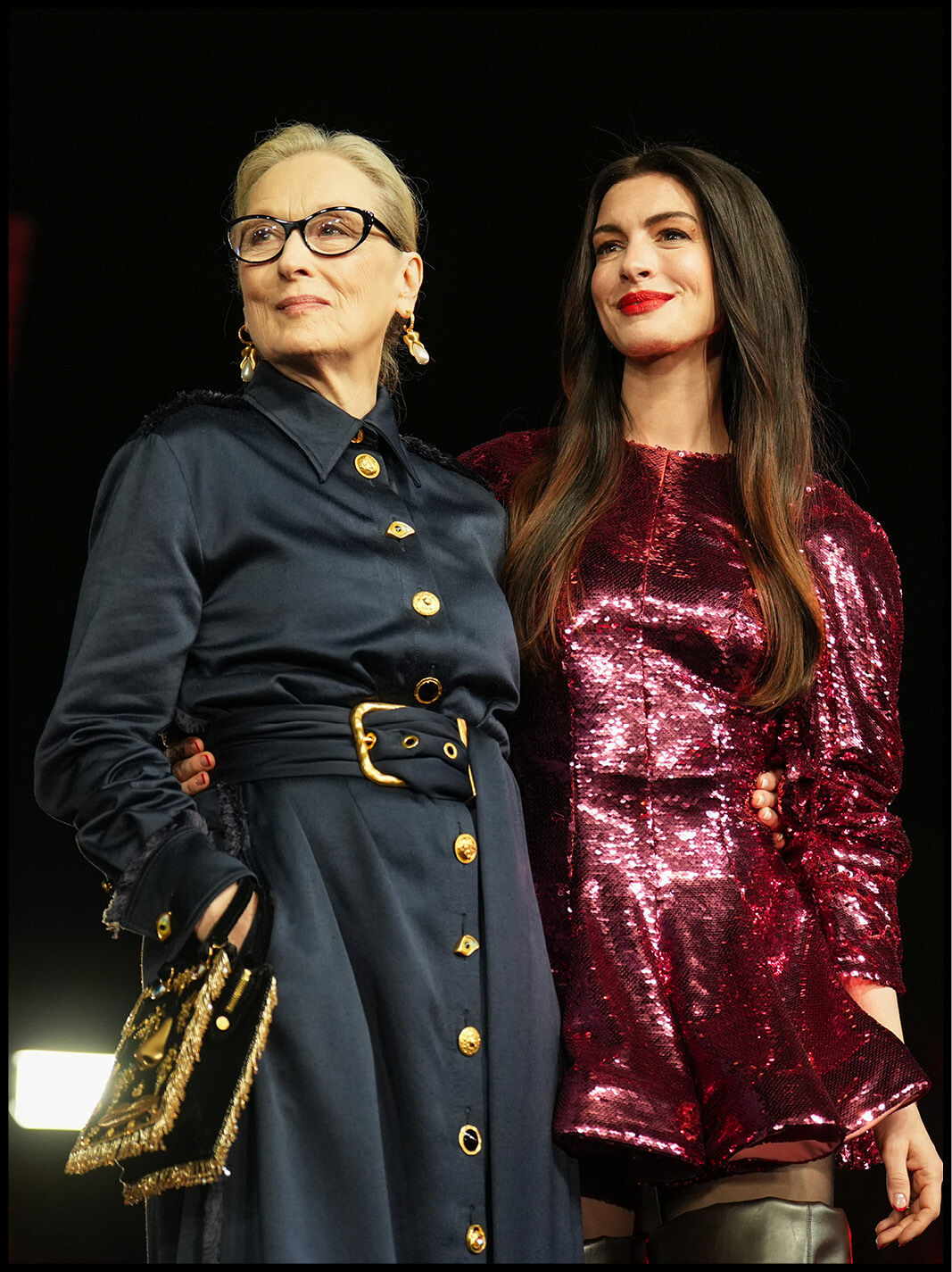 Meryl Streep and Anne Hathaway looking confidently out into the distance in their high end clothing.