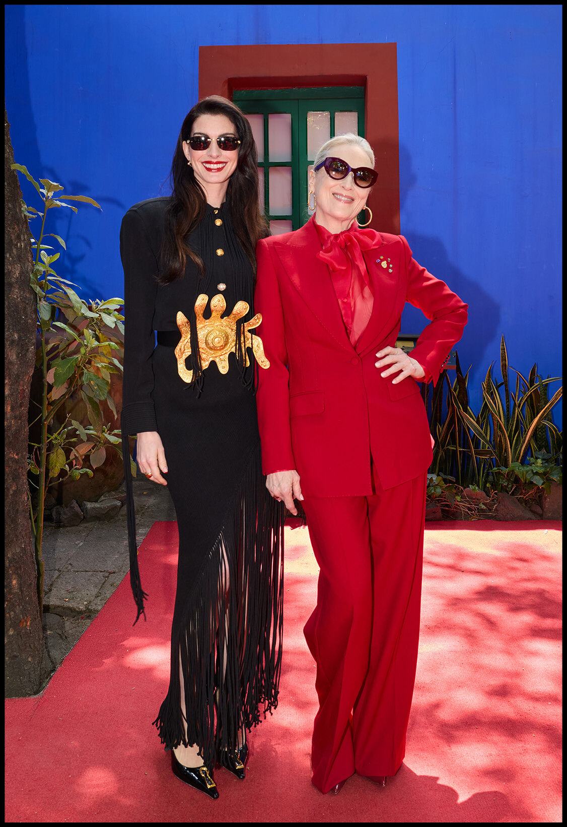 Anne Hathaway and Meryl Streep pose on a red carpet in fashionable attire.