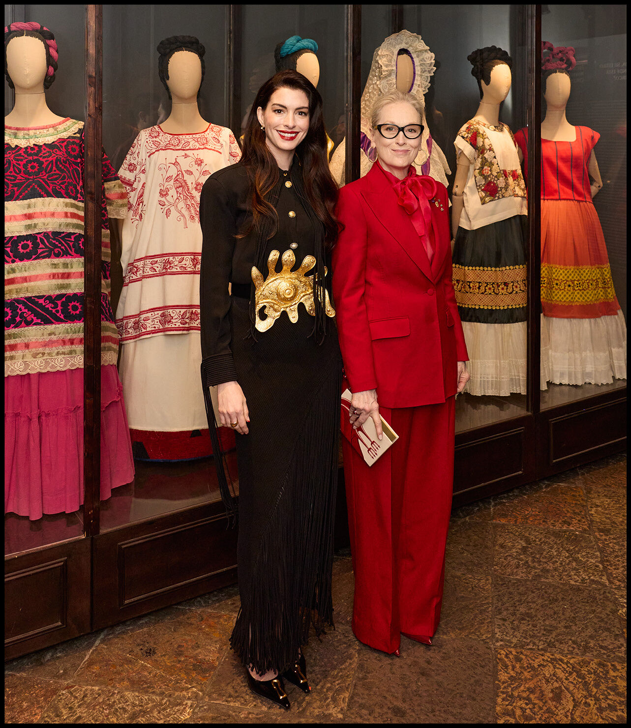 Anne Hathaway and Meryl Streep standing in front of dresses showcased at the Museo Frida Kahlo.