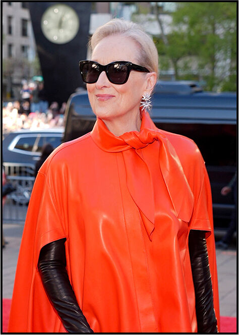 Close‑up of Meryl Streep looking to the side, highlighting her spiked statement earrings and the soft red tie detail of her cape.