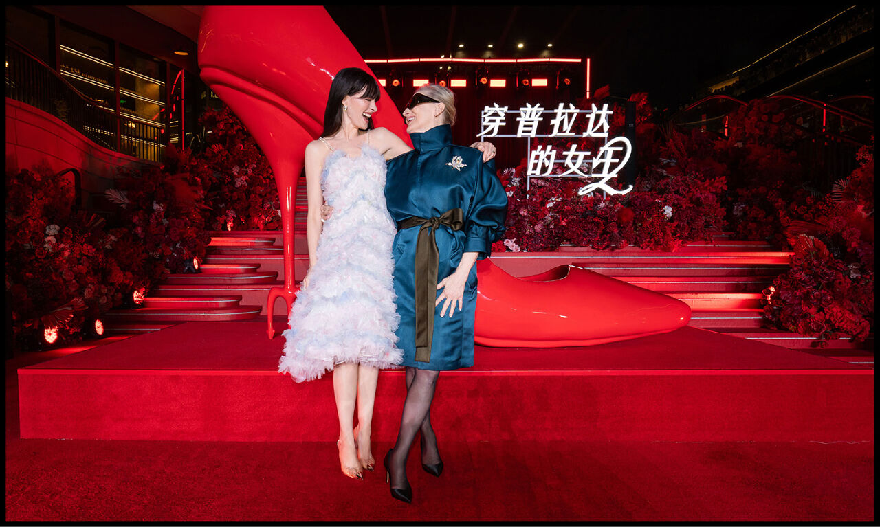 Anne Hathaway and Meryl Streep smiling at each other on the red carpet in front of the Chinese The Devil Wears Prada 2 logo.