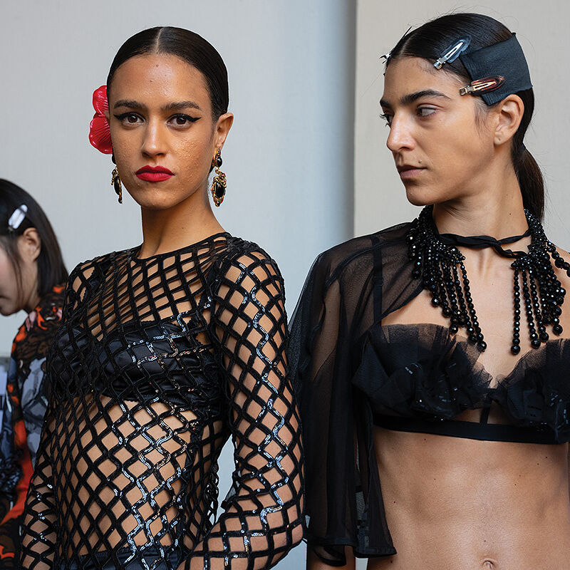 A behind-the-scenes photo essay catches a possibly tense moment between two bare-bellied models with middle parts, slicked-back hair and similar black bra tops backstage at Milan Fashion Week.