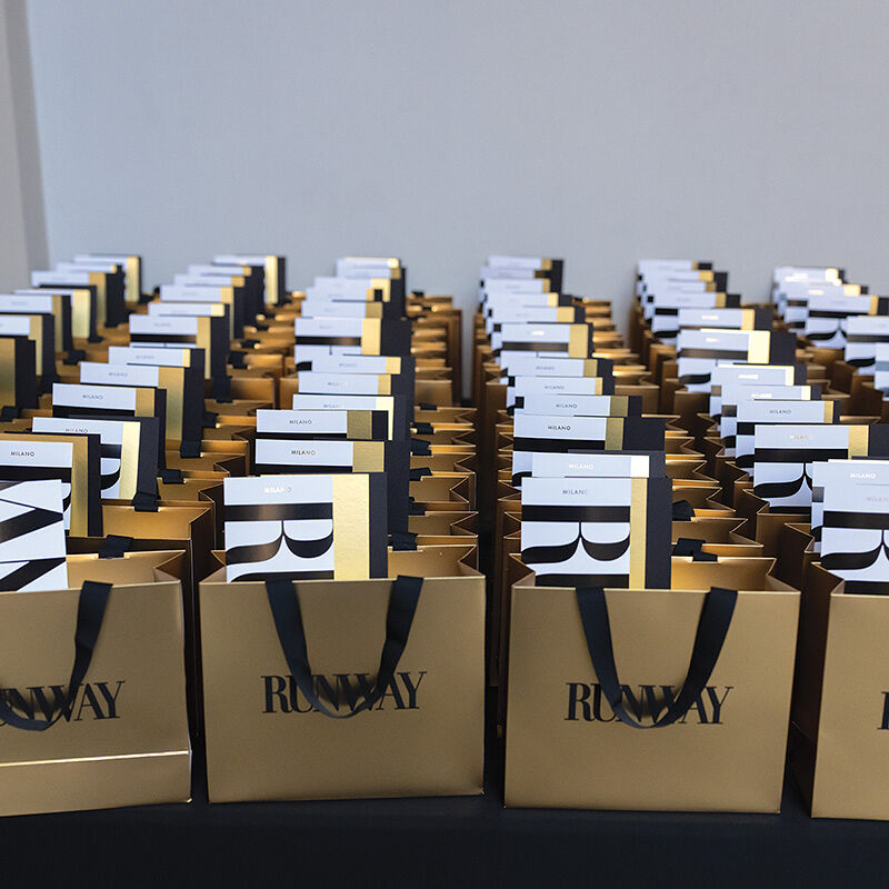 Gift bags containing seating assignments and Runway fashion show programs are lined up awaiting guest arrivals.