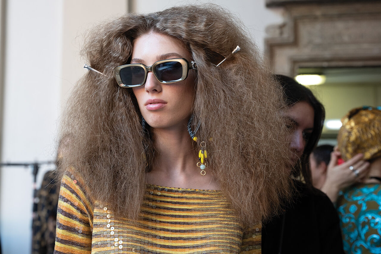 A big-haired model in gold sunglasses and giant earrings seems unfazed by the pre-catwalk chaos that occurs backstage before the big Runway magazine show at Milan Fashion Week begins.