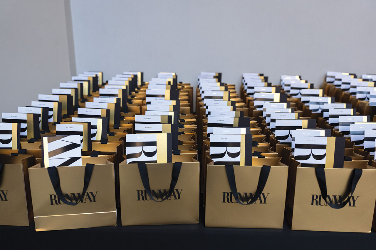 Gift bags containing seating assignments and Runway fashion show programs are lined up awaiting guest arrivals.