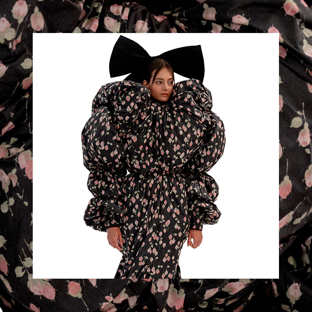 A model wears a theatrically big black and pink floral dress inspired by Victorian bustles and a giant bow in her hair to represent the nostalgic return of romance and maximalism in spring collections.