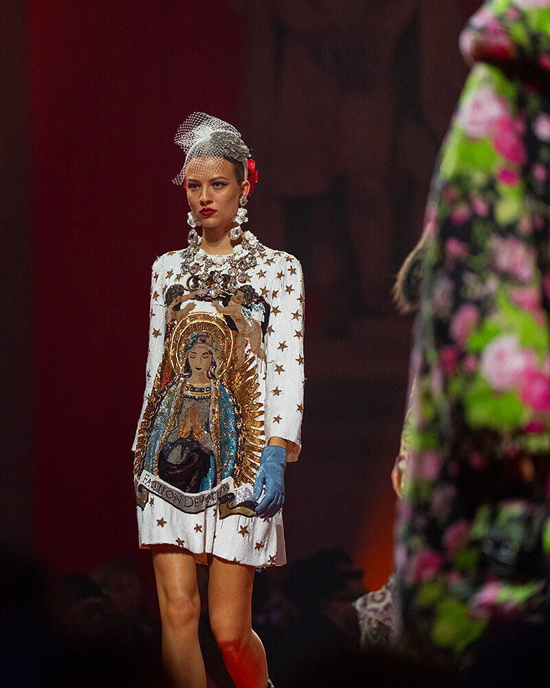 A model walks down the runway wearing a white patterned outfit.