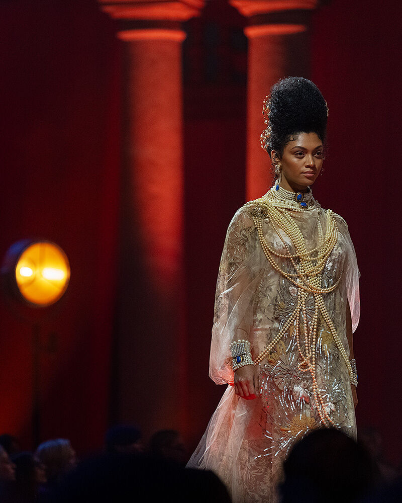 A model, adorned with pearls and gold jewelry, walks down the runway.