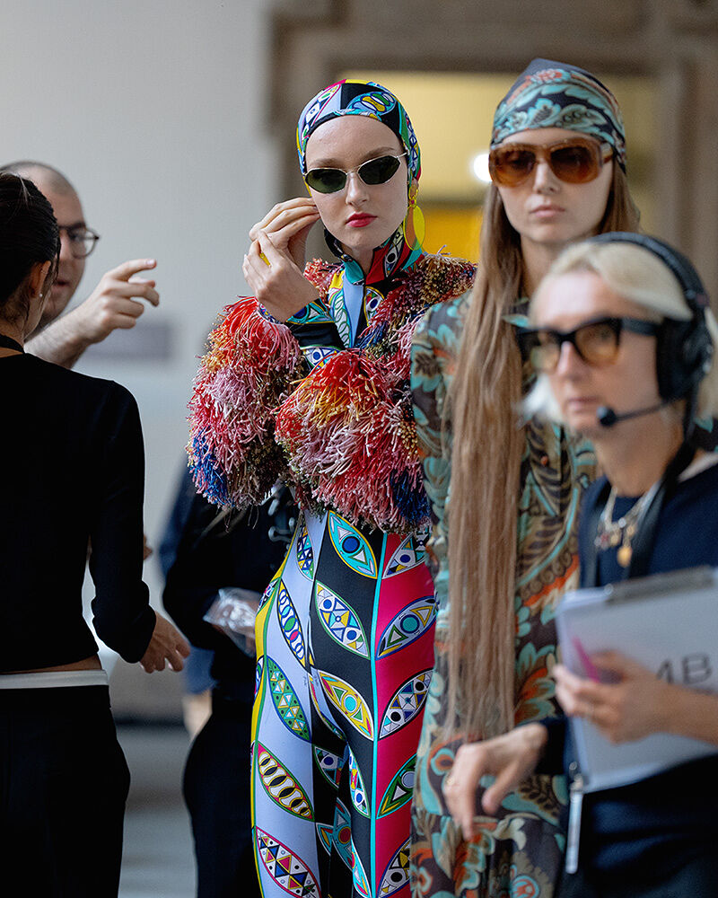 Models, dressed in a collection of patterned outfits, prepare to walk onto the runway.