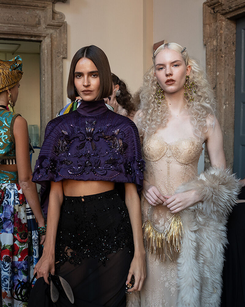 Frills, patterns, and bold accessories on display as two models prepare to walk onto the runway.