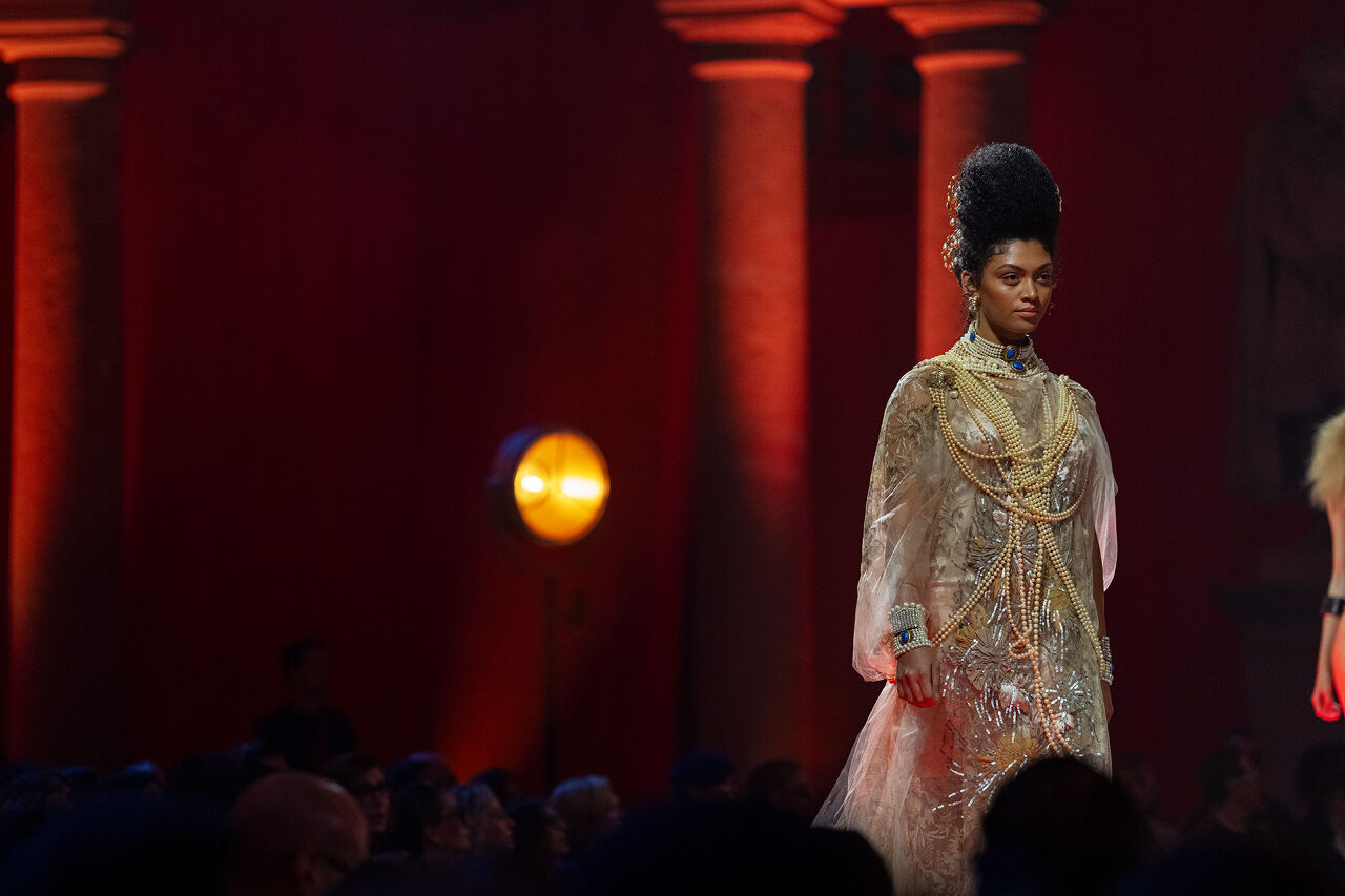 A model, adorned with pearls and gold jewelry, walks down the runway.