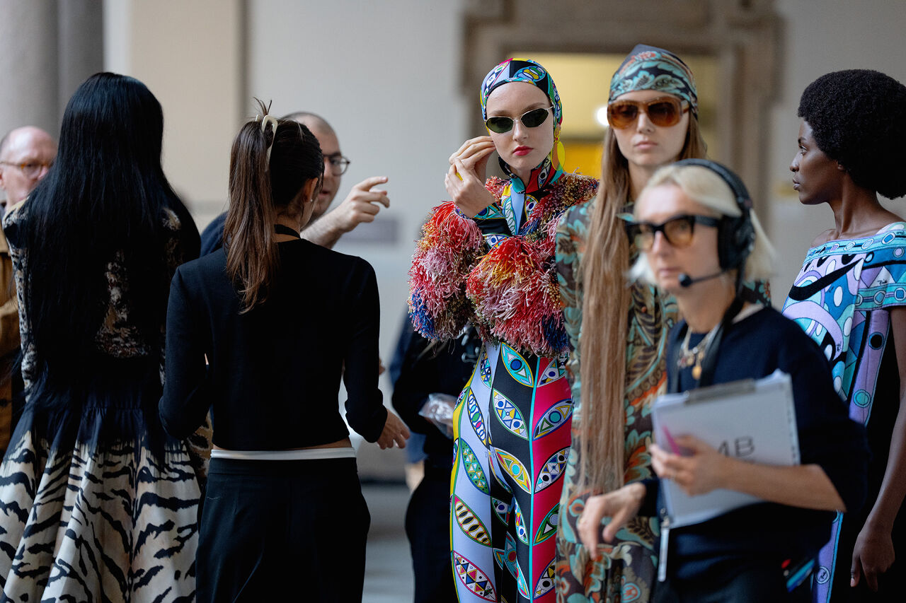 Models, dressed in a collection of patterned outfits, prepare to walk onto the runway.