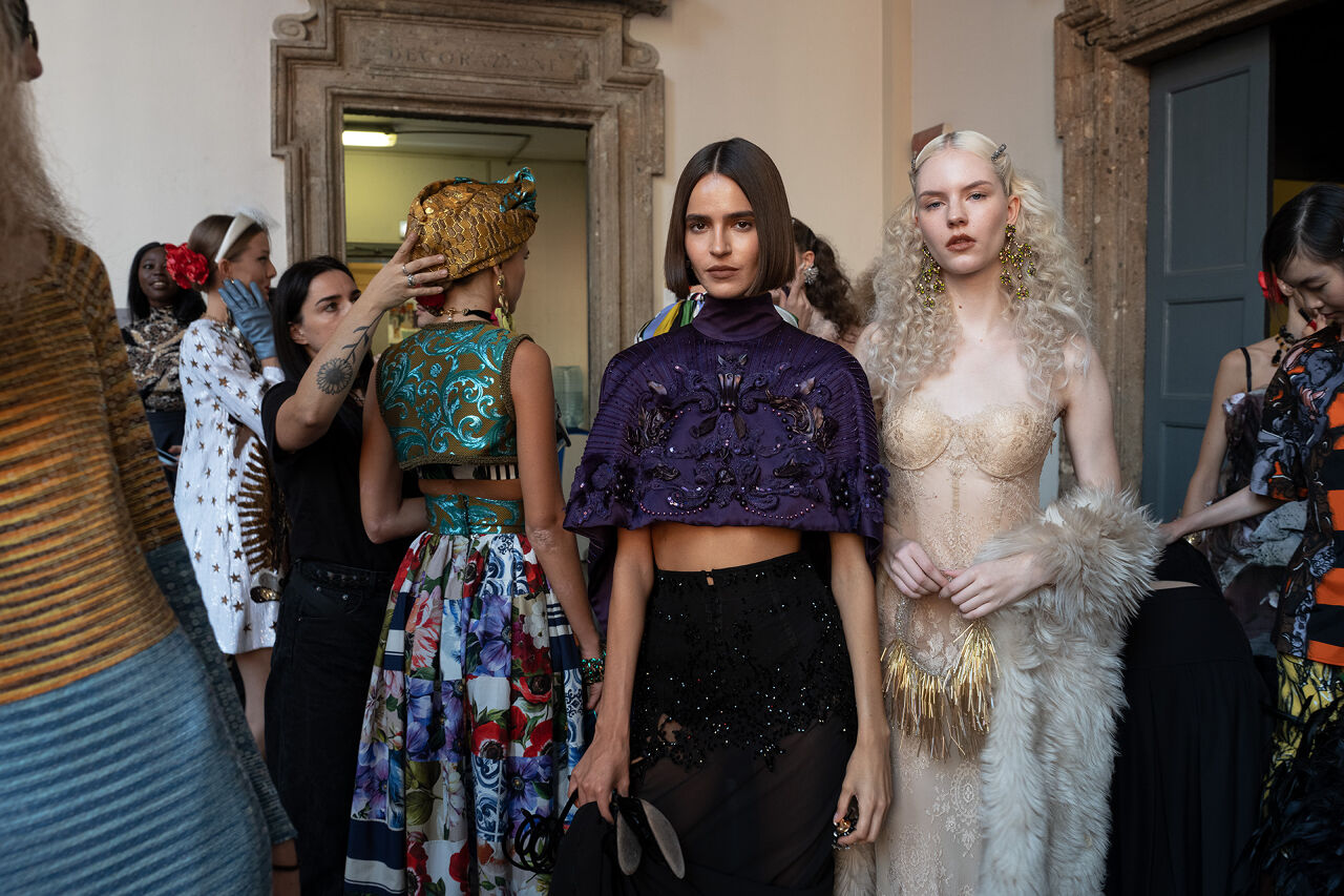 Frills, patterns, and bold accessories on display as two models prepare to walk onto the runway.