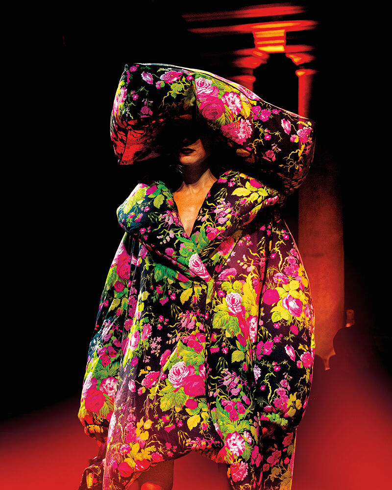 A model becomes a walking garden on the runway at Milan Fashion Week thanks to a mammoth pillow-like hat and oversized coat dress, both covered in neon blooms and foliage.