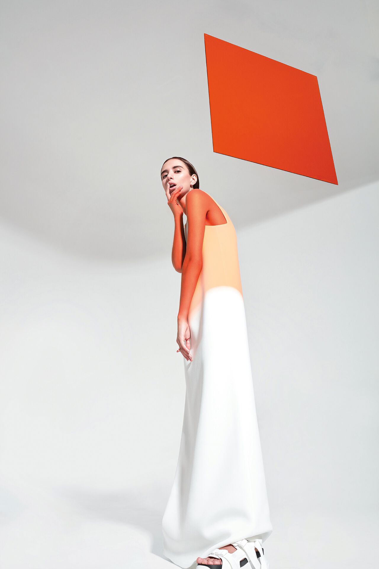 A model wears a loose simple two-tone tank dress that evokes a watercolor painting or a Creamsicle, which contrasts her arms and shoulders which have been painted a deeper shade of orange. 