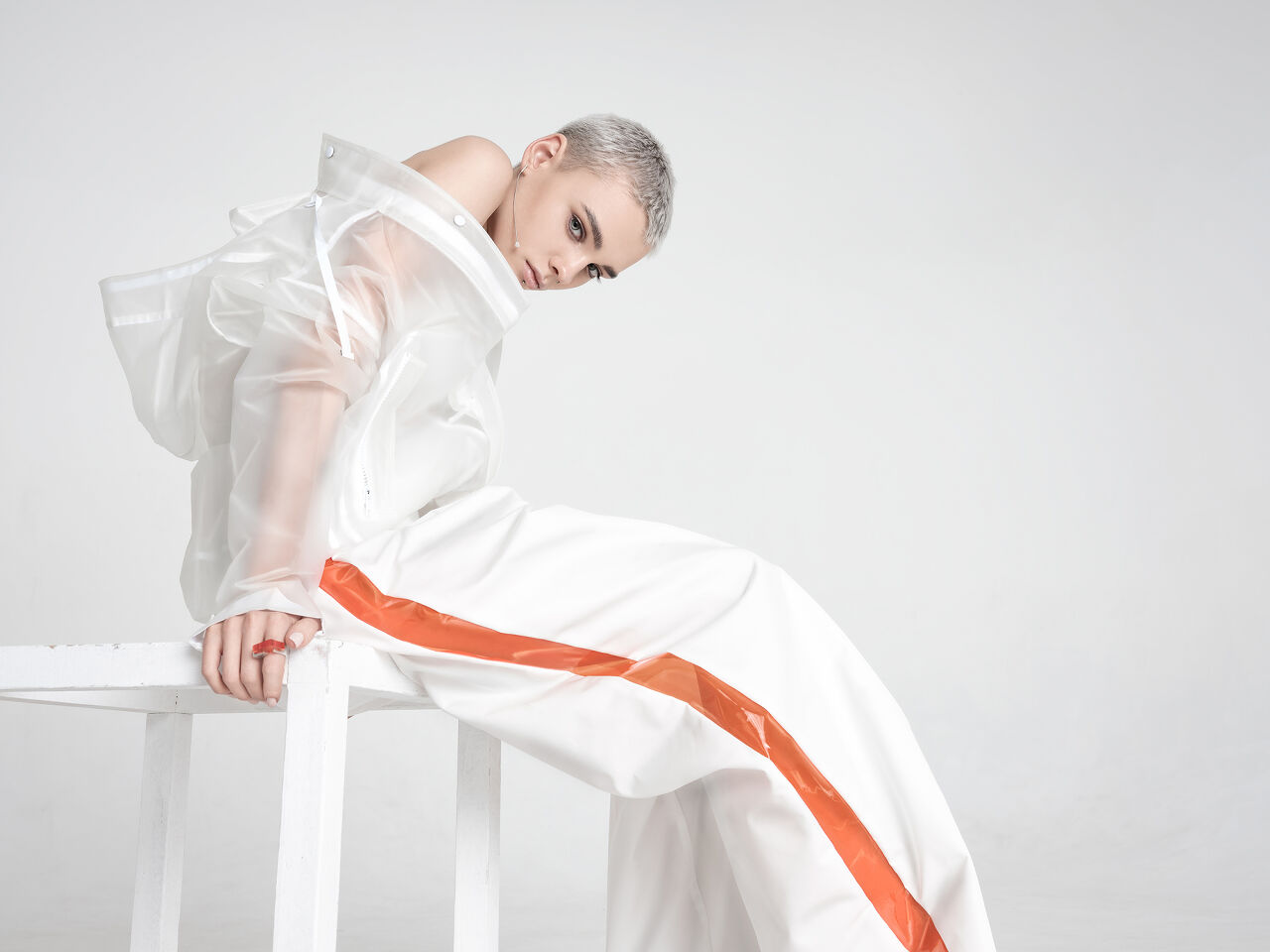 A hint of orange in the model’s ring matches the citrus streak running down the side of her perfectly baggy pants. The creamy glaze on her lips and ivory nail polish finishes the striking streetwear look.