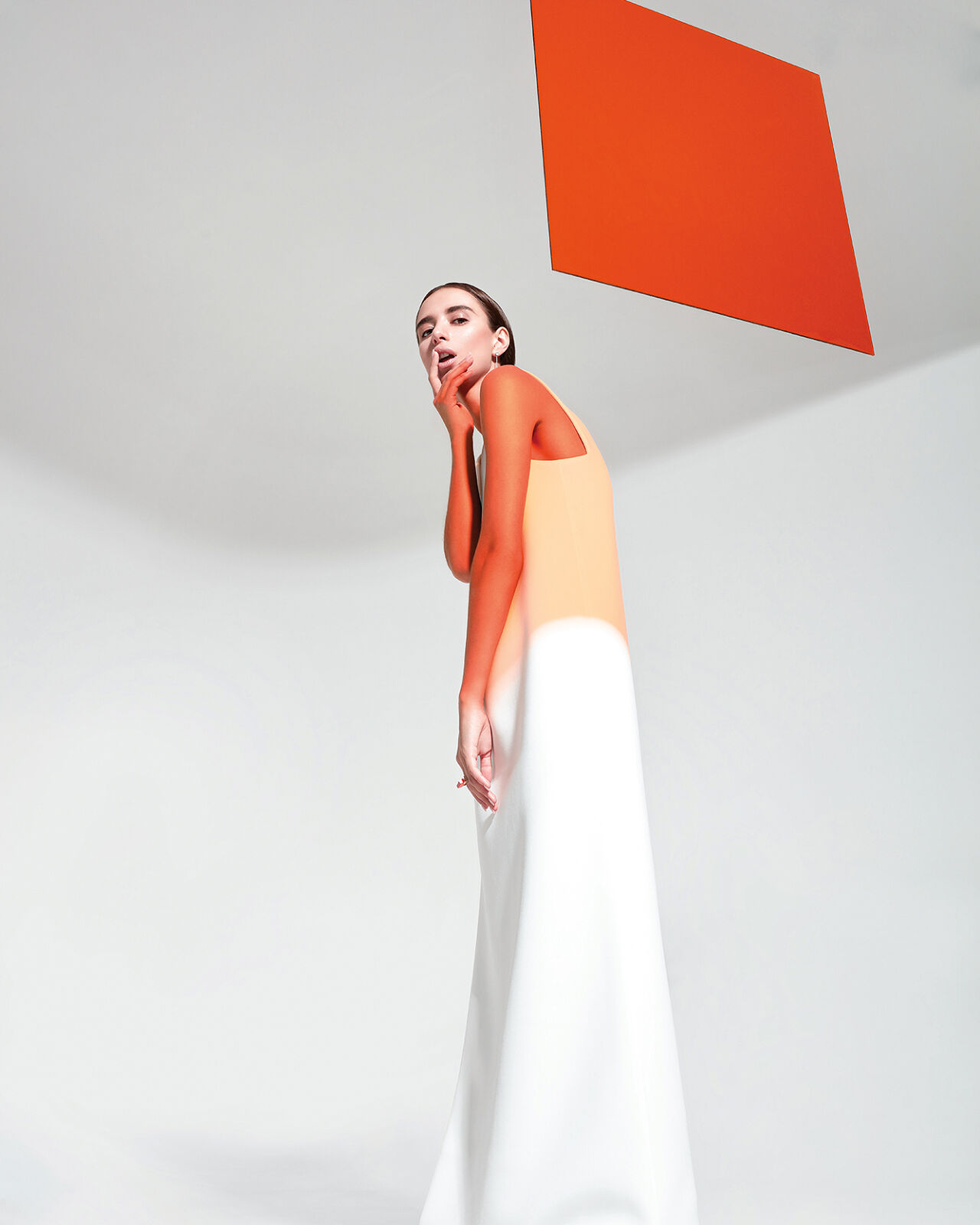 A model wears a loose simple two-tone tank dress that evokes a watercolor painting or a Creamsicle, which contrasts her arms and shoulders which have been painted a deeper shade of orange. 