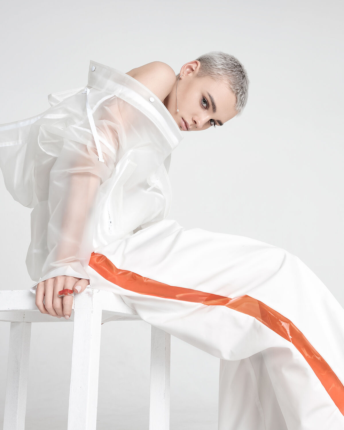 A hint of orange in the model’s ring matches the citrus streak running down the side of her perfectly baggy pants. The creamy glaze on her lips and ivory nail polish finishes the striking streetwear look.