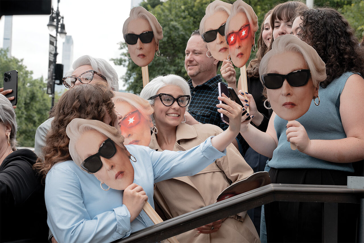 Mask-carrying fans, including a few bespectacled lookalikes, line up hours before the Runway Gala is set to begin in hopes of catching a glimpse of fashion icon Miranda Priestly.