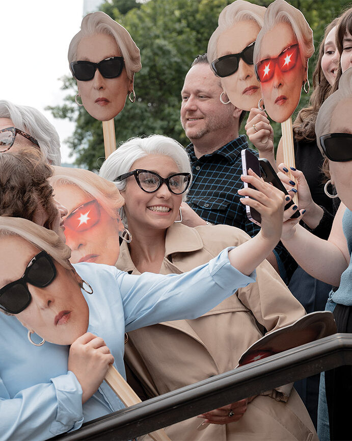 Mask-carrying fans, including a few bespectacled lookalikes, line up hours before the Runway Gala is set to begin in hopes of catching a glimpse of fashion icon Miranda Priestly.