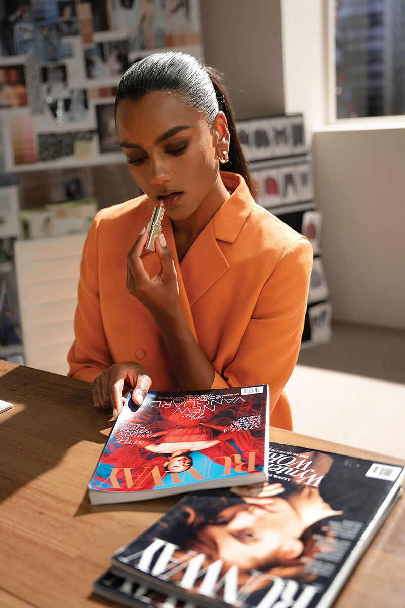 Miranda Priestly’s new first assistant Amari Mari knows the importance of multitasking. Here, she flips through past issues of Runway while reapplying her long-lasting and hydrating L'Oréal Paris cream lipstick in a shade perfectly matched to her tailored tangerine blazer.