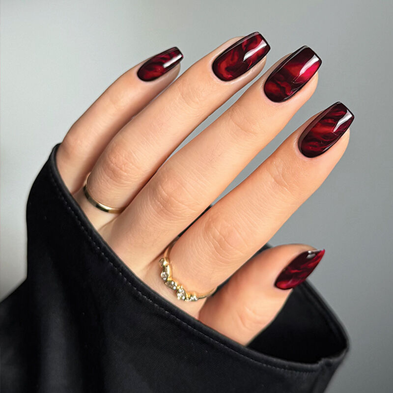 A hand peeks out from a black sleeve to reveal a red and black marbleized nail design by artist Sarah Haidar.