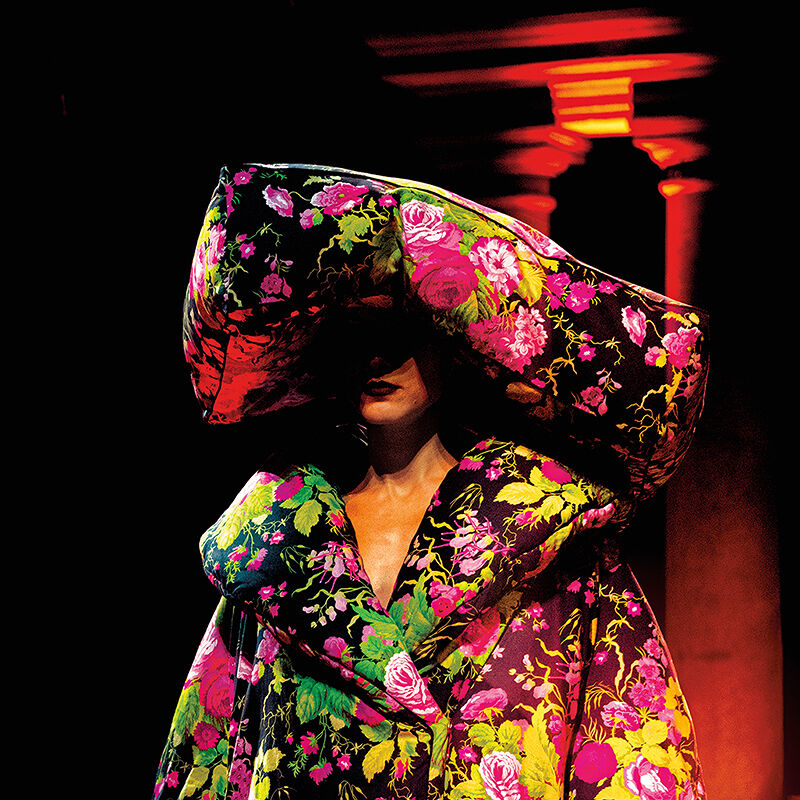 A model becomes a walking garden on the runway at Milan Fashion Week thanks to a mammoth pillow-like hat and oversized coat dress, both covered in neon blooms and foliage.