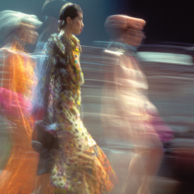 Group of models in vibrantly colored dresses walking the catwalk together in the finale of a runway show.