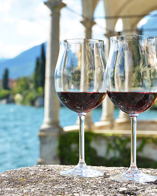 Two glasses of wine against a backdrop of the Lake Como coastline.
