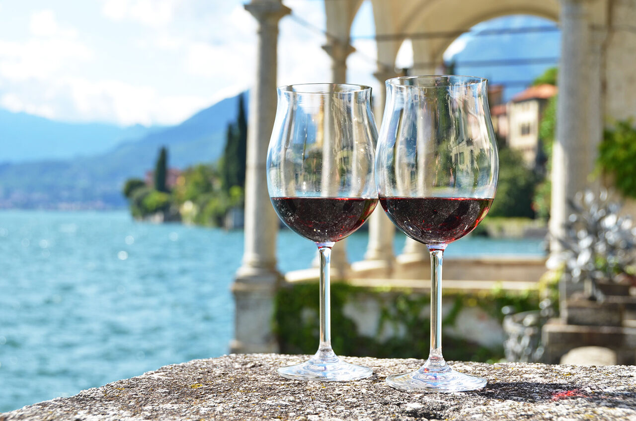 Two glasses of wine against a backdrop of the Lake Como coastline.
