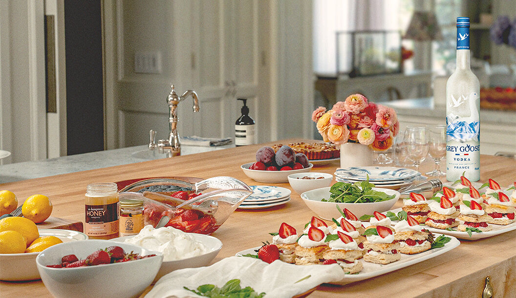 The fixings for individual strawberry shortcake desserts, served at Miranda Priestly’s seasonal brunch in the Hamptons, sit atop a butcher block kitchen island alongside the GREY GOOSE Vodka used in the signature cocktail. 