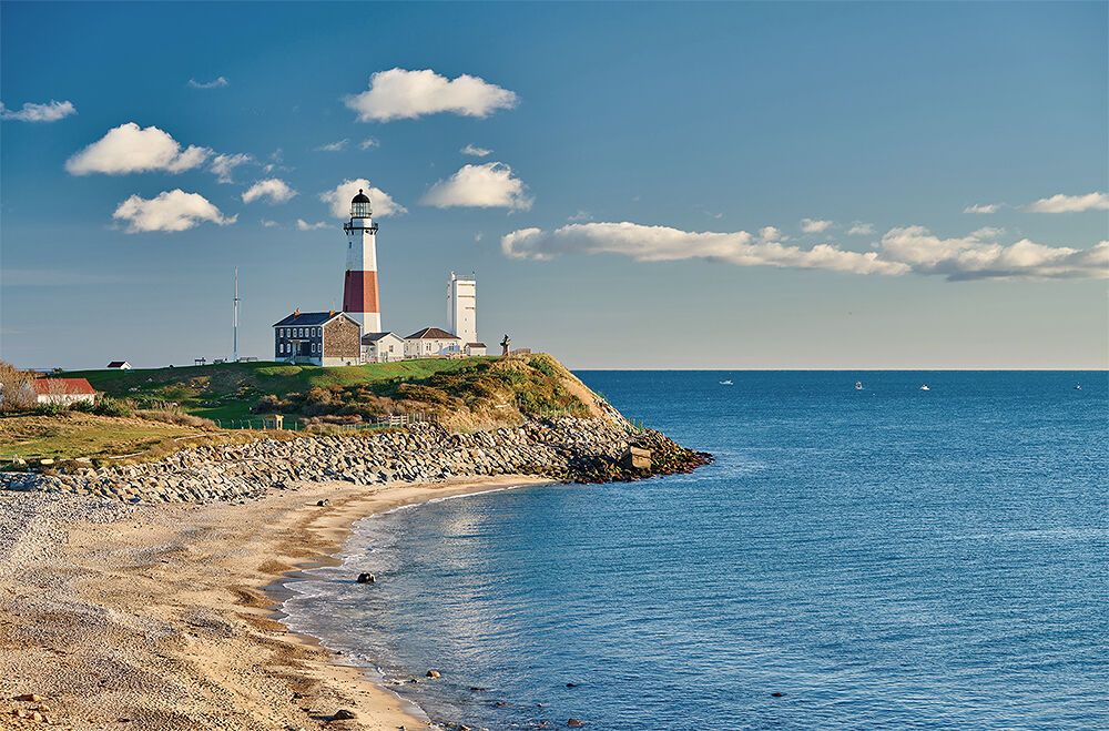 Below the Montauk Point Lighthouse in the Hamptons, the calm Atlantic waters ebb and flow while boats bob in the distance. 